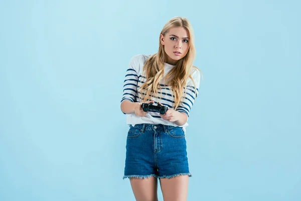 Belle fille blonde concentrée jouant à des jeux vidéo avec joystick isolé sur bleu — Photo de stock