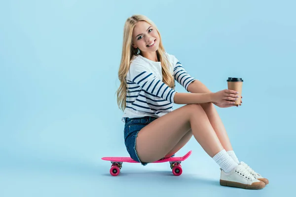 Улыбающаяся девушка с чашкой кофе, сидящая на доске на синем фоне — стоковое фото