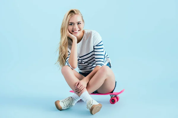 Smiling girl sitting on longboard with legs crossed on blue background — Stock Photo