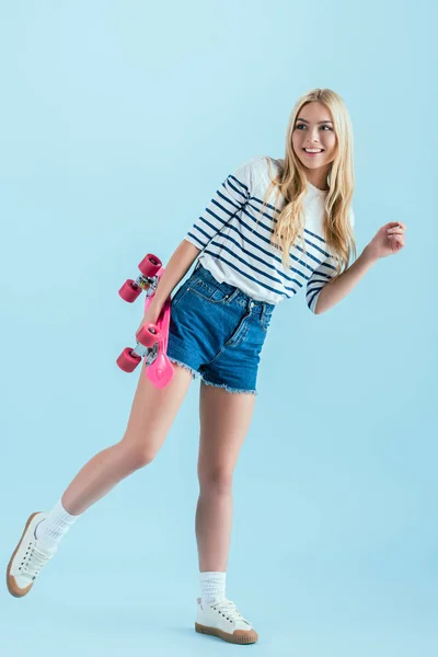 Smiling girl with longboard standing on one leg isolated on blue — Stock Photo