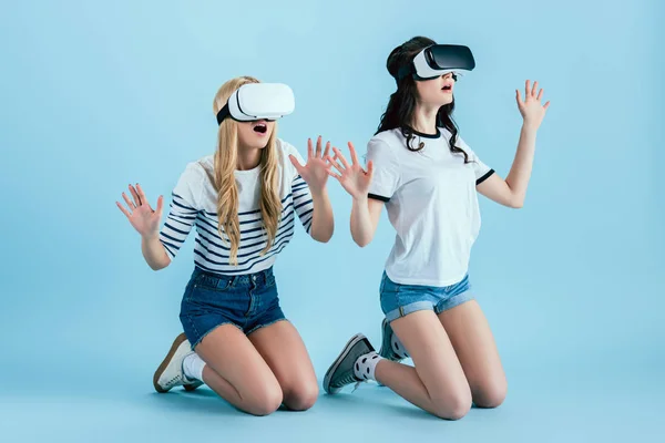 Studio shot of amazed girl in VR headset standing on knees on blue background — Stock Photo