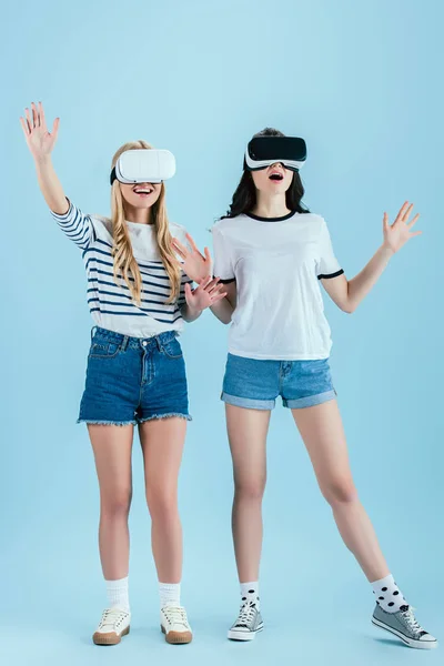 Chicas emocionadas posando en auriculares VR aislados sobre fondo azul - foto de stock