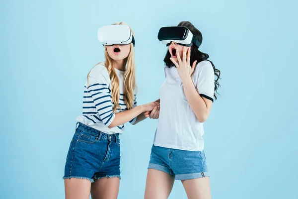Chicas conmocionadas usando auriculares de realidad virtual sobre fondo azul - foto de stock