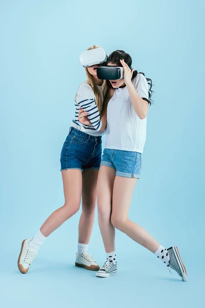 Plan studio de filles surprises dans des casques VR embrassant sur fond bleu — Photo de stock