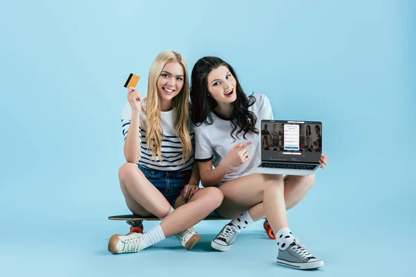 Studio shot of girls on longboard holding laptop with linkedin website on screen and credit card on blue background — Stock Photo