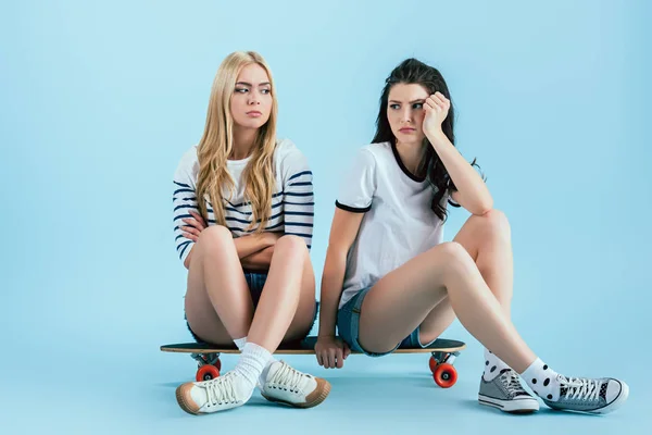 Chicas aburridas sentadas en longboard sobre fondo azul - foto de stock