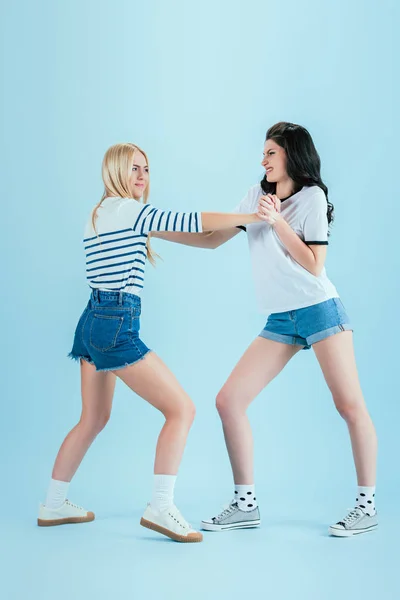 Chicas agresivas en pantalones cortos de mezclilla luchando sobre fondo azul - foto de stock