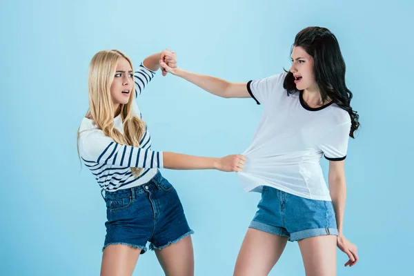 Mujeres jóvenes irritadas luchando sobre fondo azul - foto de stock