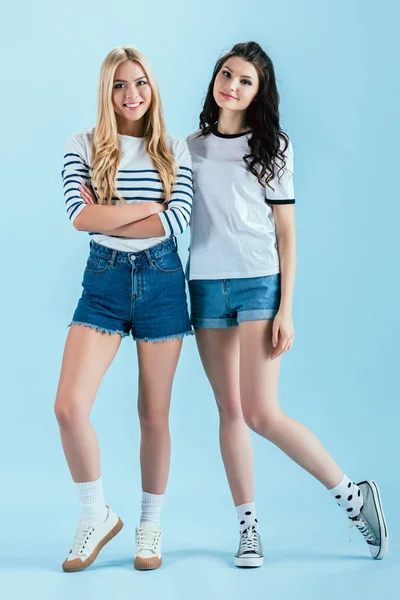 Cheerful girls in denim shorts looking at camera on blue background — Stock Photo