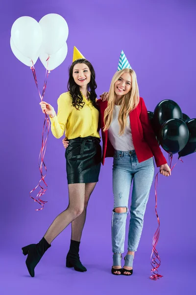 Studio shot of smiling girls with balloons embracing on purple background — Stock Photo