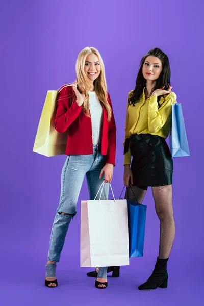 Meninas bonitas segurando sacos de compras coloridos no fundo roxo — Fotografia de Stock