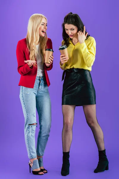 Chicas alegres hablando mientras beben café sobre fondo morado - foto de stock