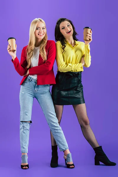 Studio shot of excited girls holding disposable cups with coffee on purple background — Stock Photo