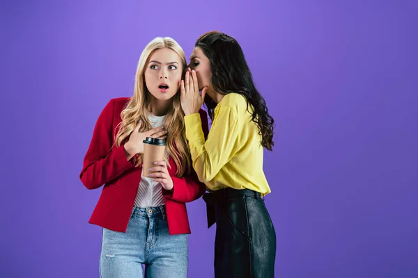 Brunette girl wishpering secret in friend's ear on purple background — Stock Photo