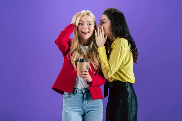 Stylish brunette woman whispering secret to friend on purple background — Stock Photo