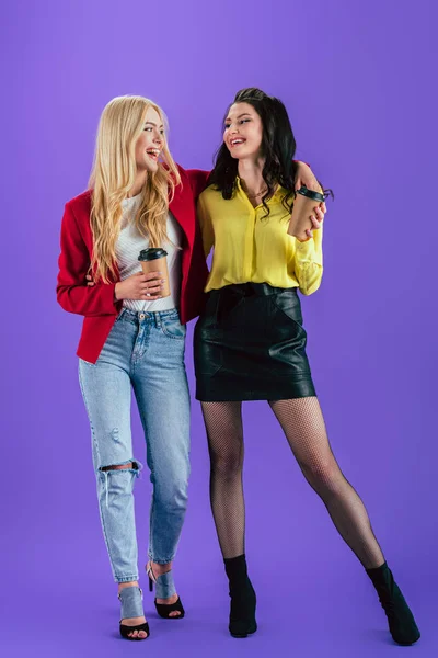 Joyful girls with coffee cups embracing on purple background — Stock Photo