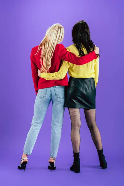 Back view of stylish women embracing on purple background — Stock Photo