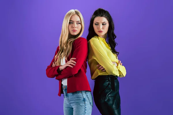 Upset young women posing with crossed arms on purple background — Stock Photo