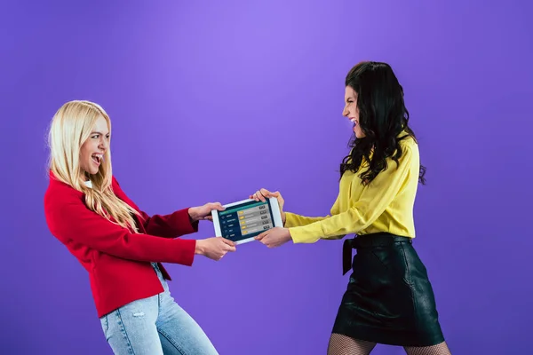 Plan studio de filles hurlantes tenant tablette numérique avec application paris sportifs à l'écran sur fond violet — Photo de stock