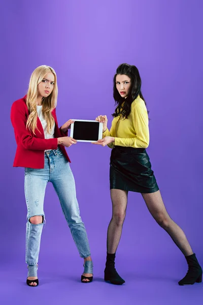 Вид в полный рост раздраженных девушек, держащих цифровую табличку с экраном-бланком на фиолетовом фоне — стоковое фото