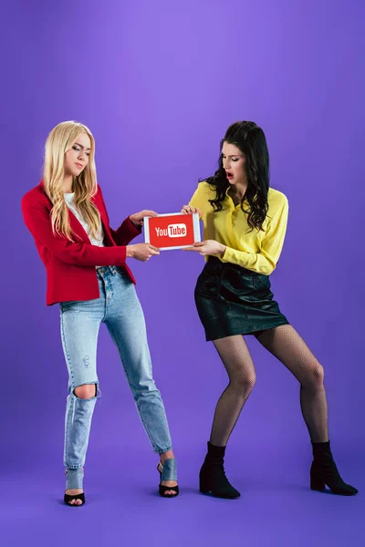 Несчастные девушки держат цифровой планшет с приложением youtube на экране на фиолетовом фоне — стоковое фото
