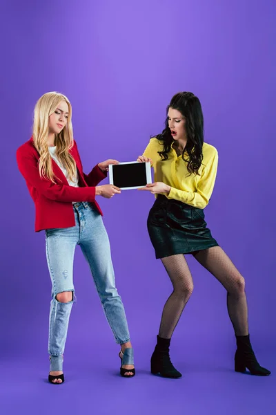 Estudio de chicas insatisfechas sosteniendo tableta digital con pantalla en blanco sobre fondo púrpura - foto de stock