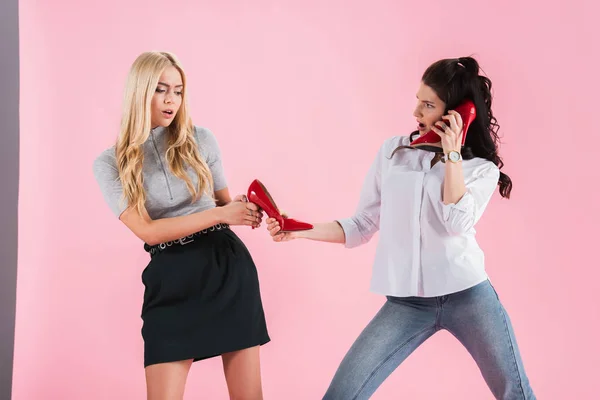 Aggressive girls fighting for stylish red shoes on pink background — Stock Photo