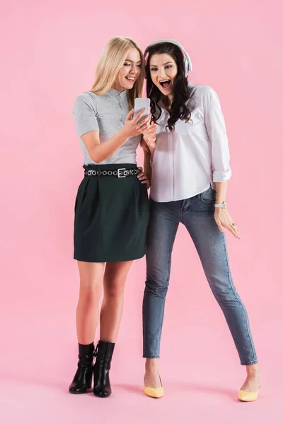 Estudio de chicas emocionadas con smartphone y auriculares escuchando música sobre fondo rosa — Stock Photo