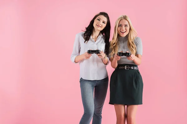 Chicas emocionadas con joysticks jugando videojuego aislado en rosa - foto de stock