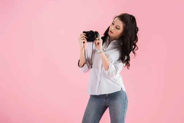 Estudio de mujer joven y curiosa con cámara digital aislada en rosa - foto de stock