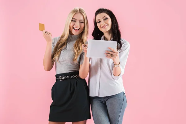 Chicas riendo con tarjeta de crédito utilizando tableta digital aislado en rosa - foto de stock