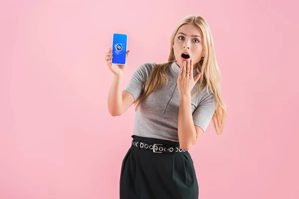 Schöne schockierte Mädchen zeigt Smartphone mit Shazam-App auf dem Bildschirm, isoliert auf rosa — Stockfoto