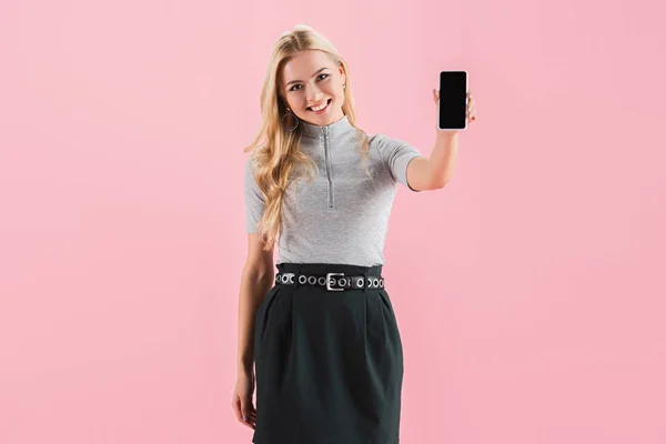 Красива щаслива дівчина, що показує смартфон з порожнім екраном, ізольована на рожевому — стокове фото