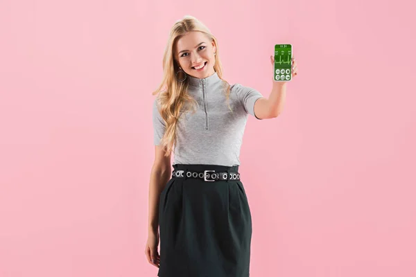 Sorrindo menina loira mostrando smartphone com dados de saúde na tela, isolado em rosa — Fotografia de Stock