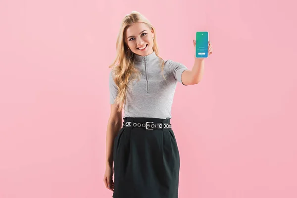 Belle fille souriante montrant smartphone avec application twitter à l'écran, isolé sur rose — Photo de stock