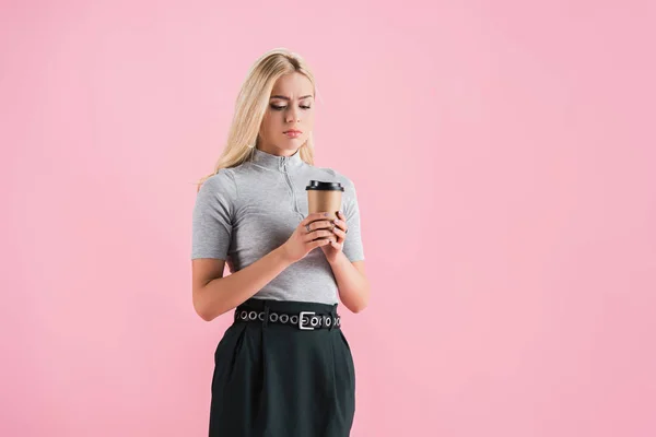 Verwirrtes blondes Mädchen beim Blick auf Coffee to go, isoliert auf rosa — Stockfoto