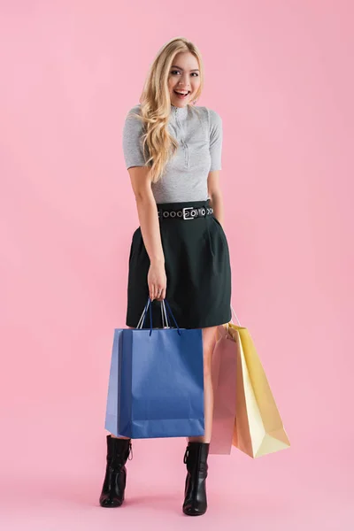 Alegre chica rubia sosteniendo bolsas de compras, aislado en rosa - foto de stock