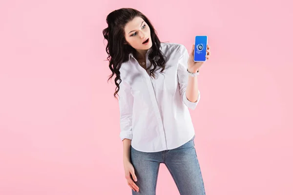 Attraktives überraschtes Mädchen zeigt Smartphone mit Shazam-App auf dem Bildschirm, isoliert auf rosa — Stockfoto