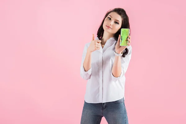 Menina bonita mostrando polegar para cima e smartphone com aplicativo de compras na tela, isolado em rosa — Fotografia de Stock