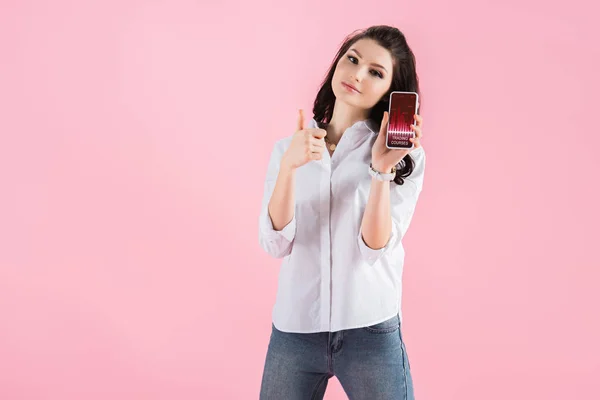 Schönes Mädchen zeigt Daumen hoch und Smartphone mit Handelskursen auf dem Bildschirm, isoliert auf rosa — Stockfoto