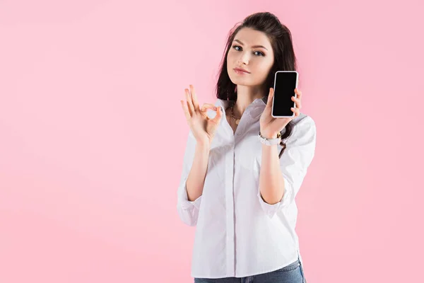 Morena mujer mostrando teléfono inteligente con pantalla en blanco y signo de ok, aislado en rosa - foto de stock