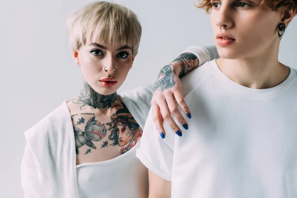 Chica tatuada de pie con el hombre aislado en gris - foto de stock