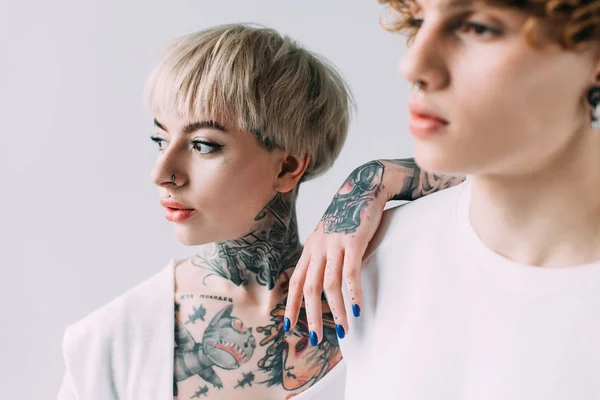 Enfoque selectivo de la mujer tatuada de pie con el hombre aislado en gris - foto de stock