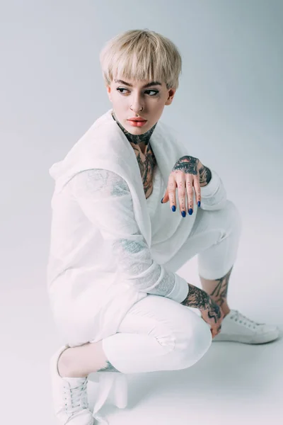 Блондинка з татуюваннями сидить на сірому фоні — стокове фото
