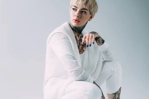 Atractiva mujer con tatuajes sentado aislado en gris - foto de stock