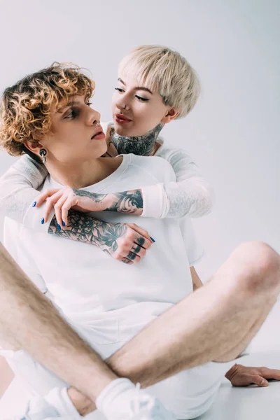 Cheerful girl hugging boyfriend with curly hair isolated on grey — Stock Photo