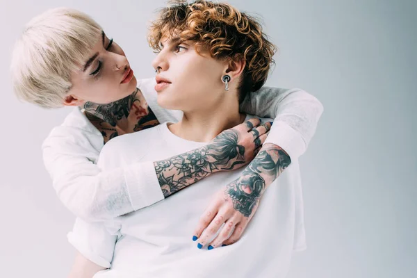 Fille blonde avec des tatouages regardant petit ami aux cheveux bouclés isolé sur gris — Photo de stock