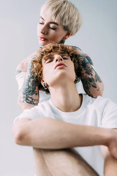 Woman with closed eyes hugging handsome boyfriend with curly hair isolated on grey — Stock Photo