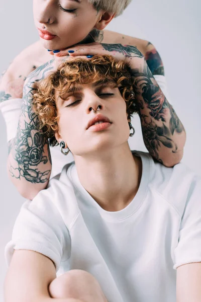 Жінка з татуюваннями кладе руки на кучеряве волосся хлопця ізольовано на сірому — стокове фото