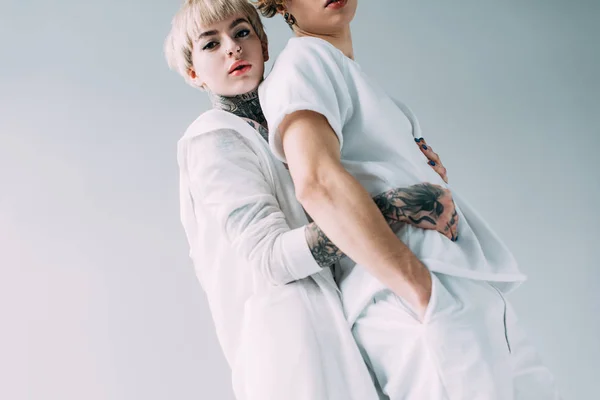 Blonde Freundin mit Tätowierungen umarmt Freund isoliert auf grau — Stockfoto